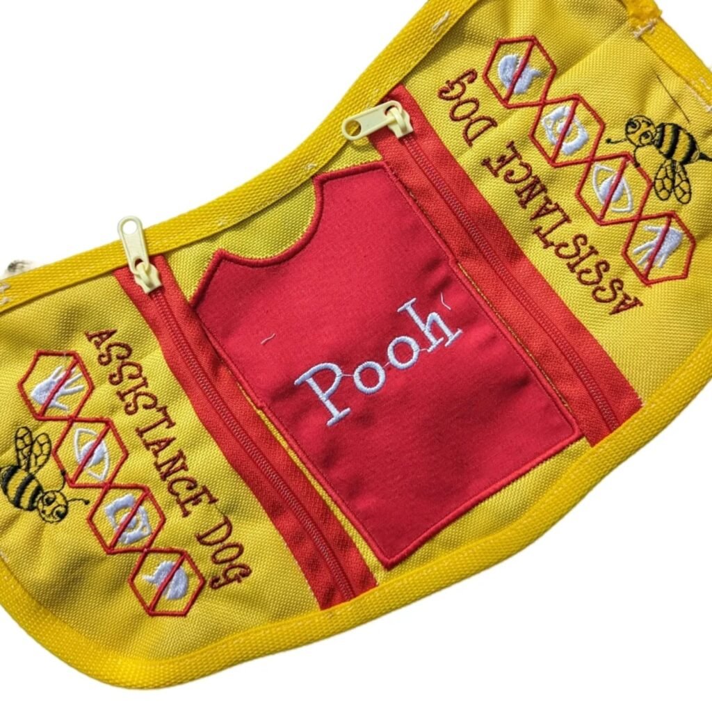 This red and yellow cape, featuring colours from the beloved Winnie the Pooh and the iconic shirt, clearly states "Assistance Dog" and includes icons to show no touching or engaging.